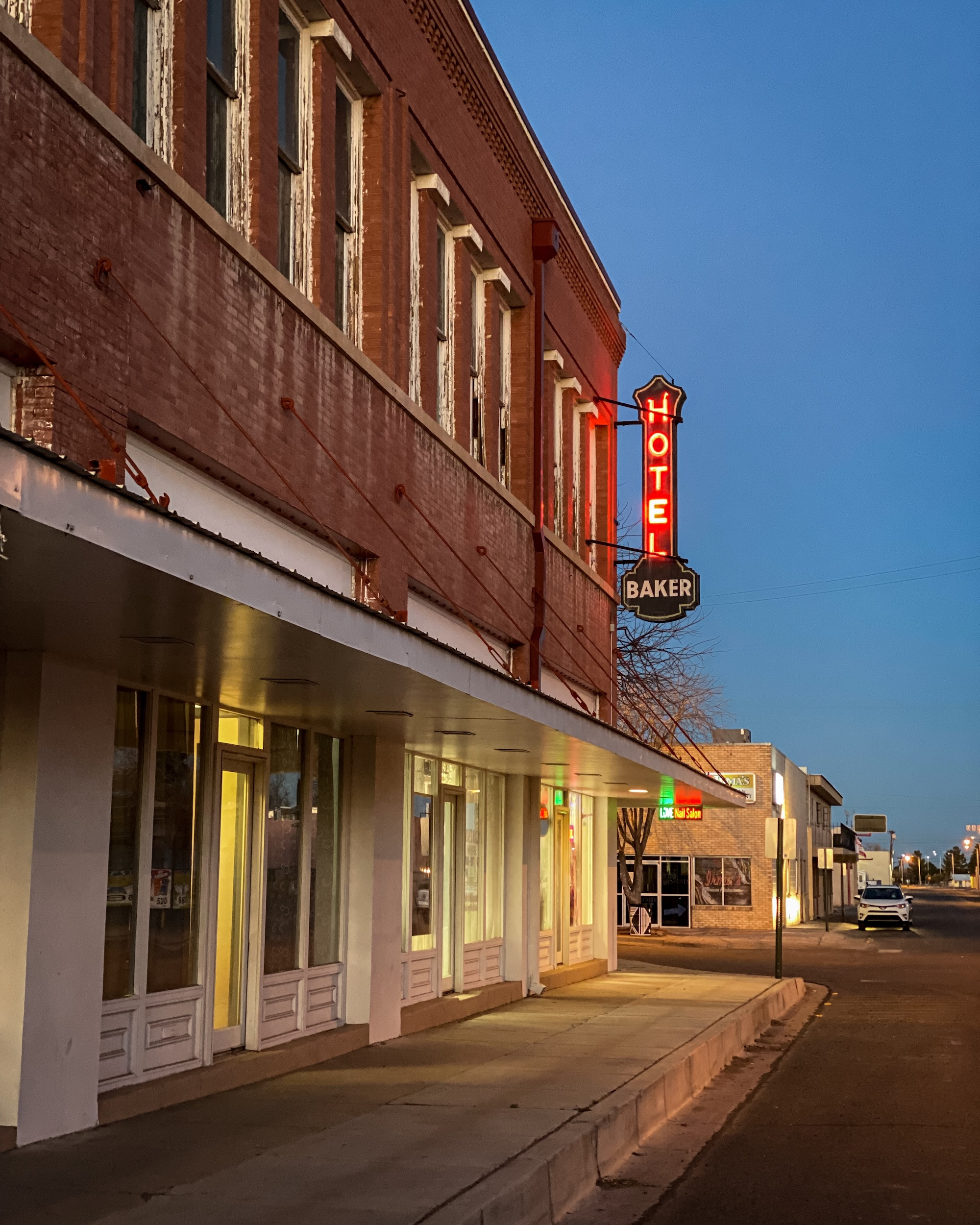 Hotel Street A glowing hotel sign beside a brick facade and quiet street at blue hour.